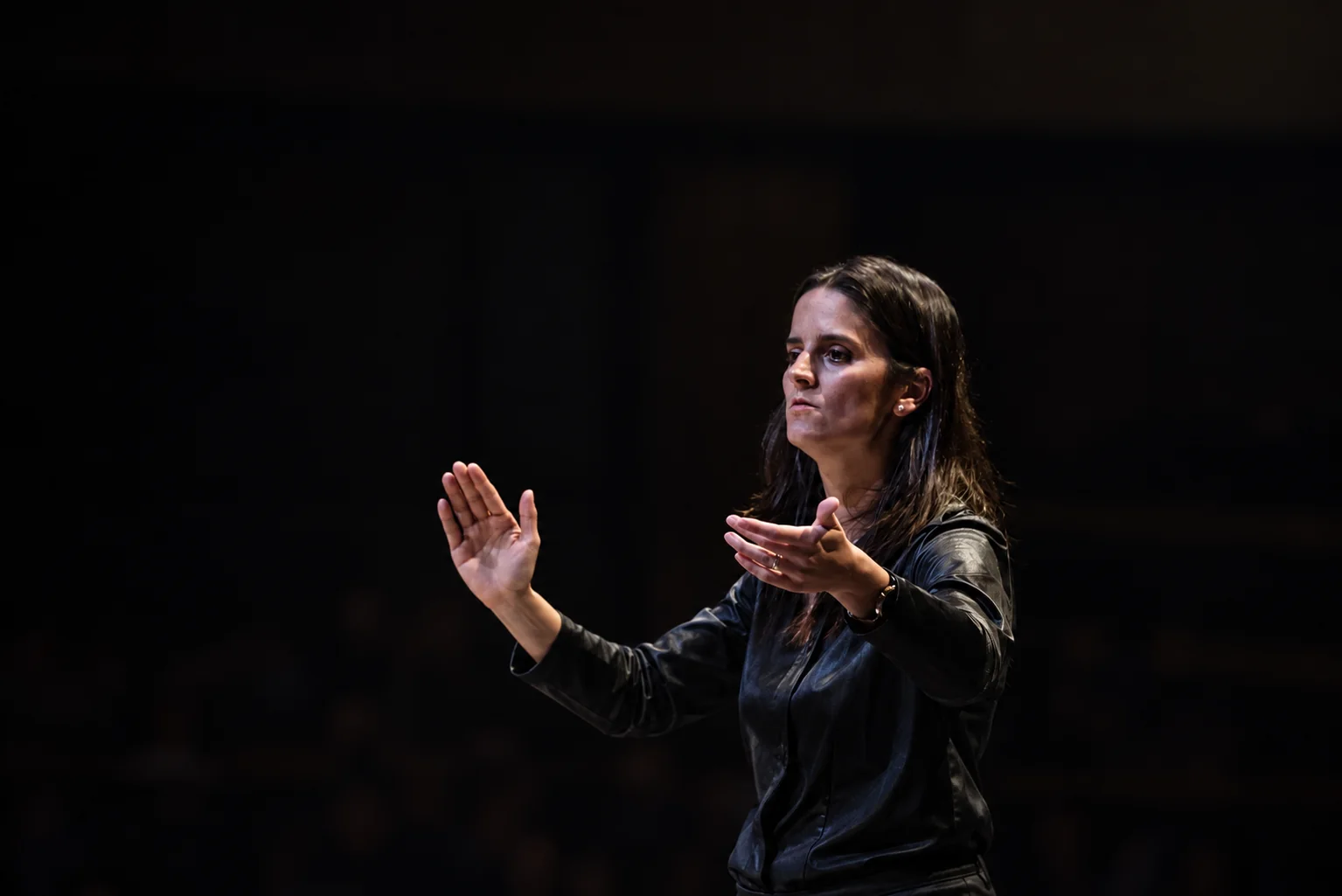 Romina Romay conducting an orchestra, her hands raised in a musical gesture